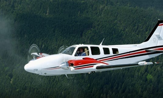 A small plane flying through the air over trees.