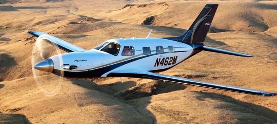 A small white plane flying over the desert.